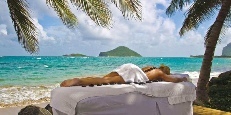 Woman relaxing with a hot stone treatment on the beach at Coconut Bay Beach Resort & Spa