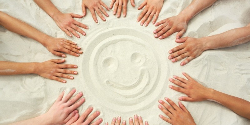 people place their hands around a face drawn in the sand on a beach