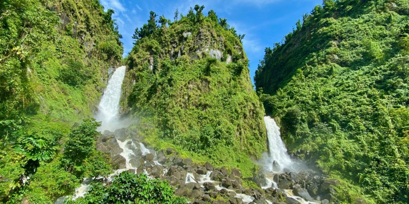 Green cliff faces with waterfalls cascading down them on to jagged rocks