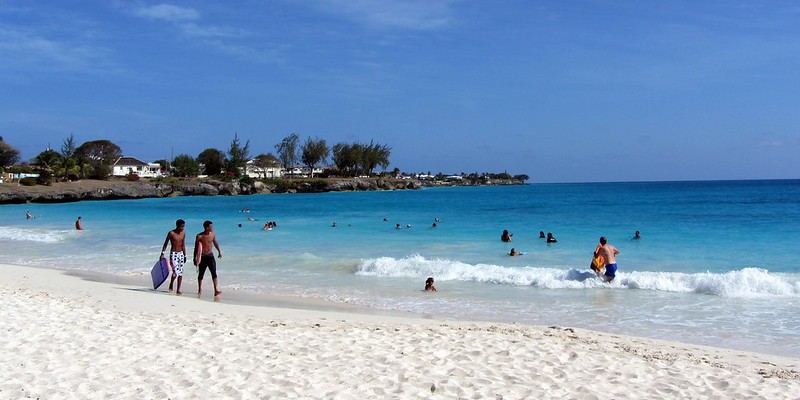 People walk on the sand and play in the sea at Miami (or Enterprise) Beach in Oistins, Barbados.