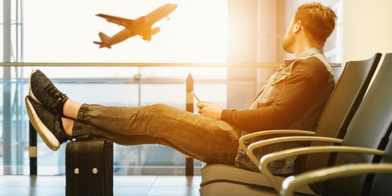 Man sitting in an airport looking out the window at a plane taking off