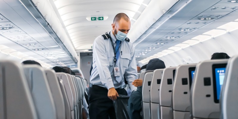 Flight attendant collecting litter on a plane with a face covering on