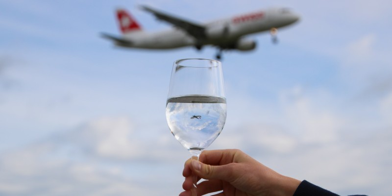 a person holding a glass of liquid with a plane flying in the distance