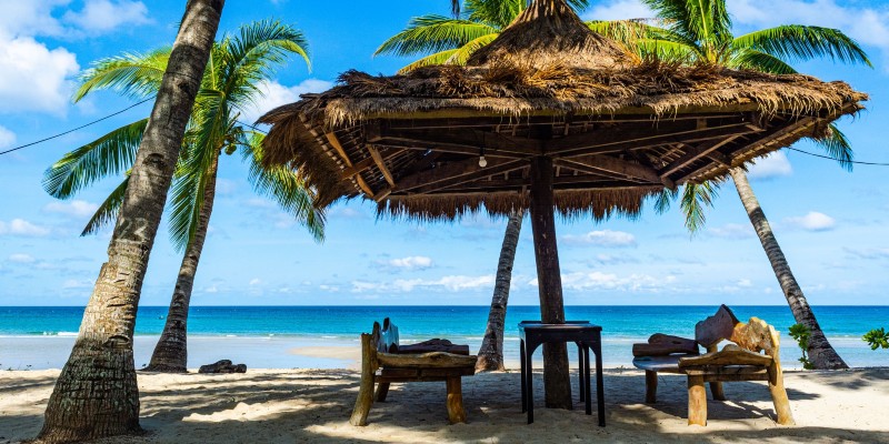 Tables and benches underneath a thatched parasol on a Caribbean beach