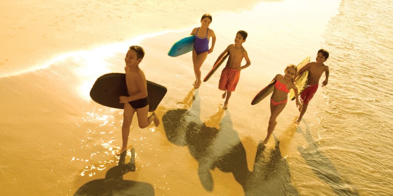 five children with surfboards run on a beach 