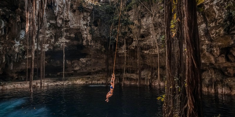 Woman swinging off a vine into a cenote