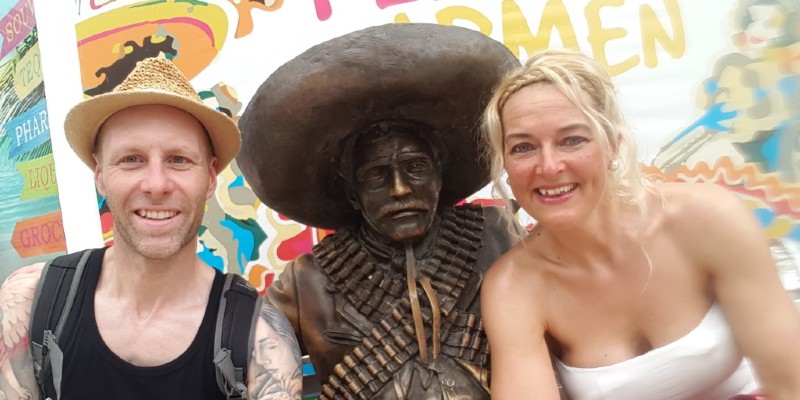 Couple posing with a statue of a man wearing a sombrero in Playa del Carmen